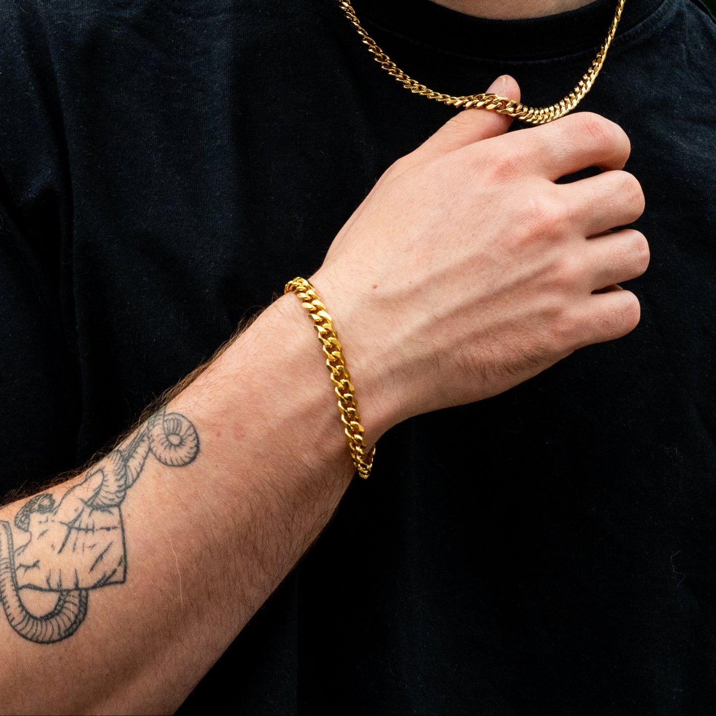 Man wearing a gold chain necklace and bracelet against a green leafy background
