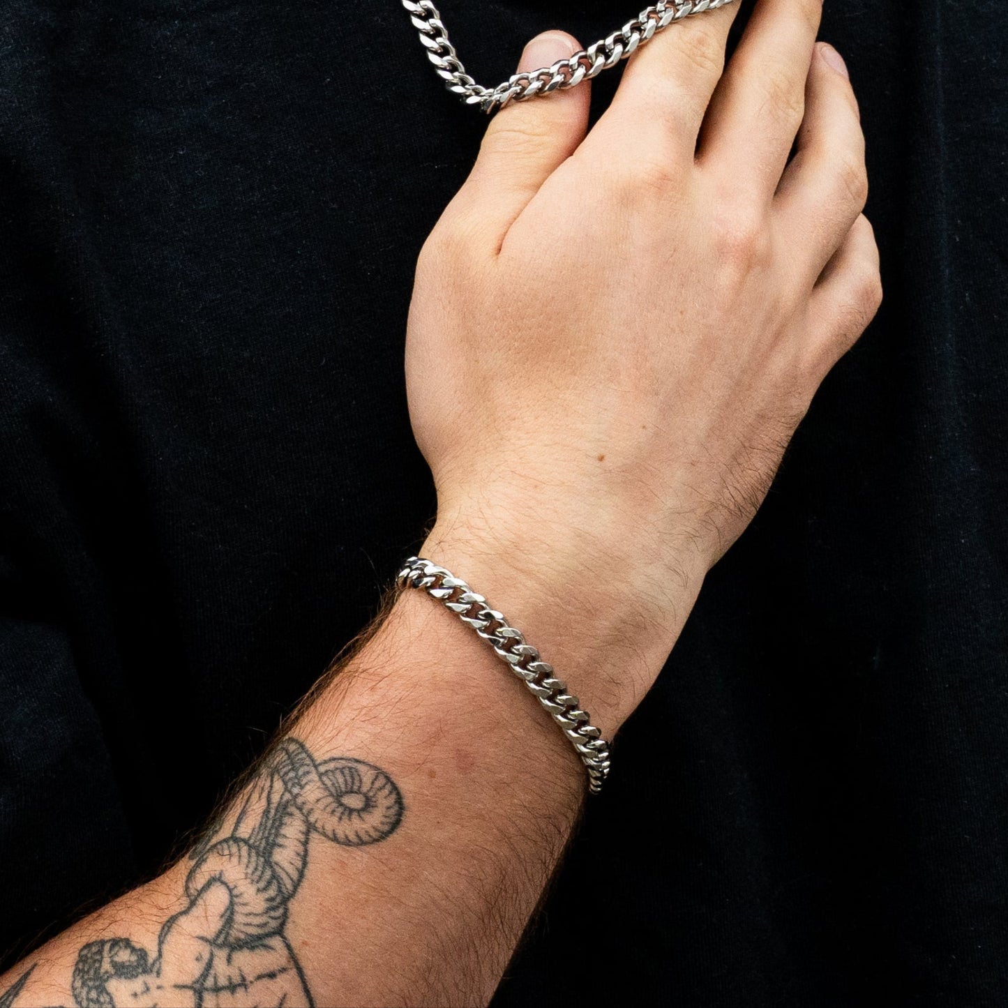 Person wearing a silver chain necklace and bracelet against a green outdoor background