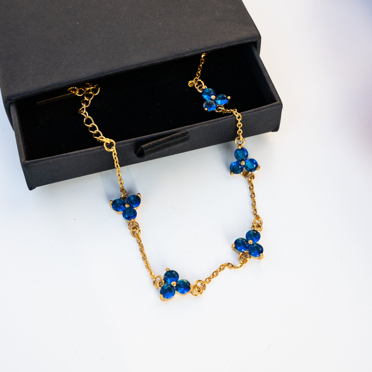 Gold necklace with blue gemstones on a surface with a box.