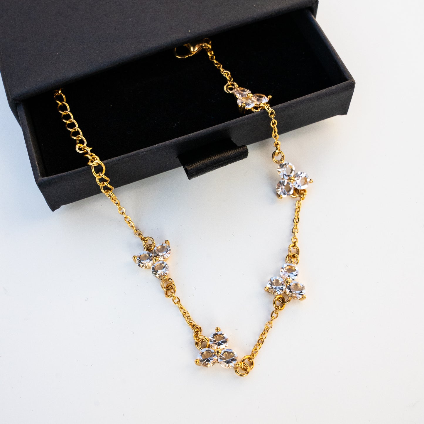 Gold necklace with crystal accents on a white surface with a box in the background