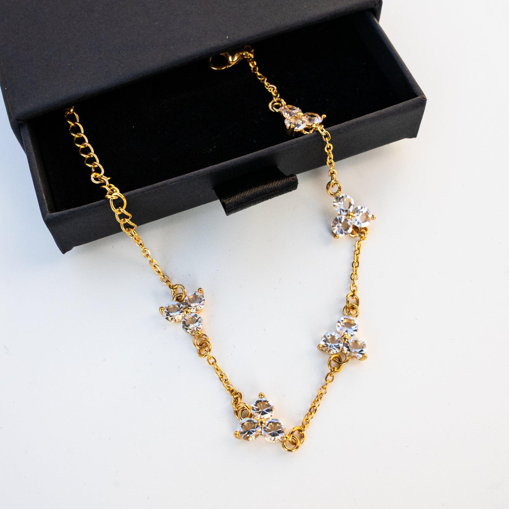Gold necklace with crystal accents on a white surface with a box in the background