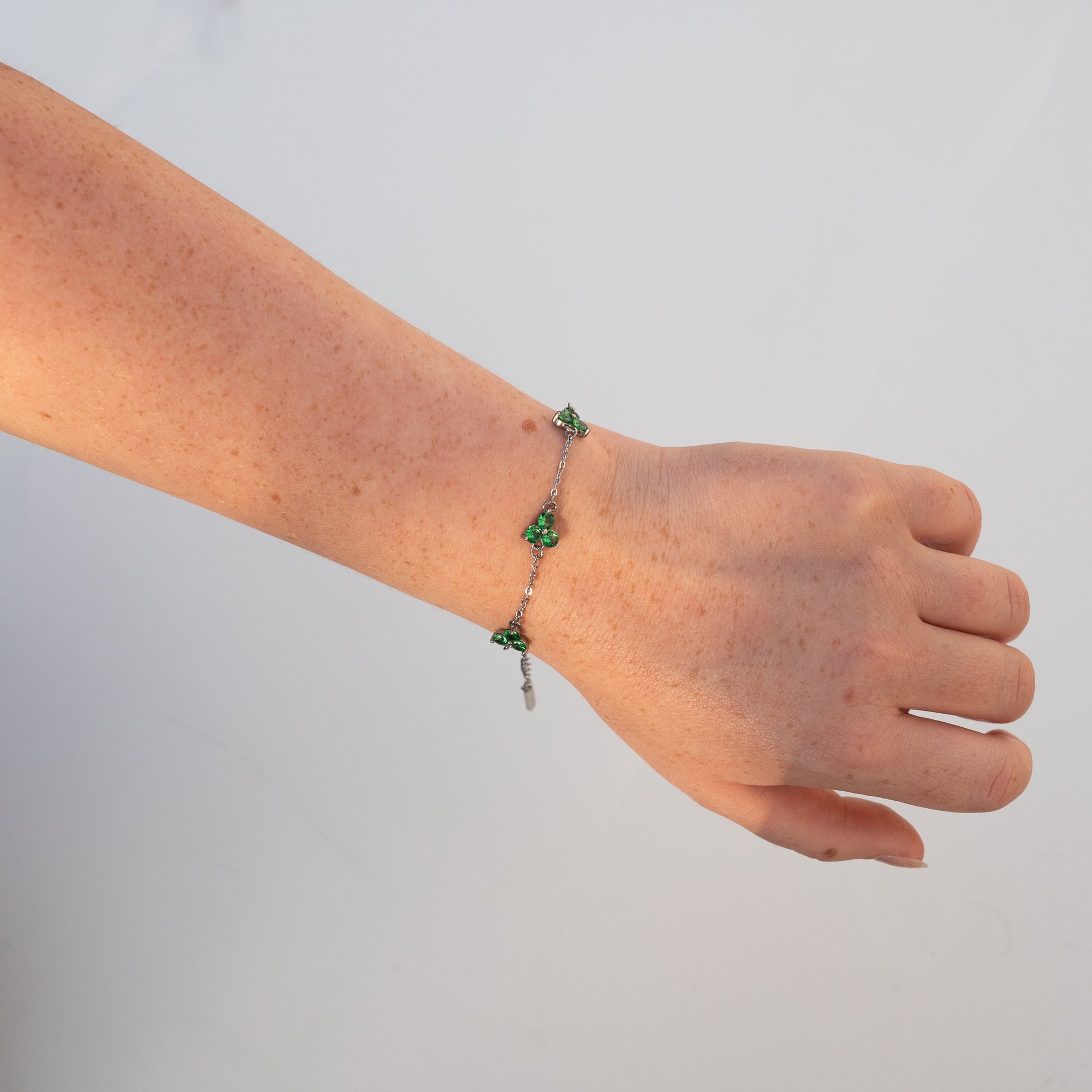 Hand wearing a silver bracelet with green stones on a plain background