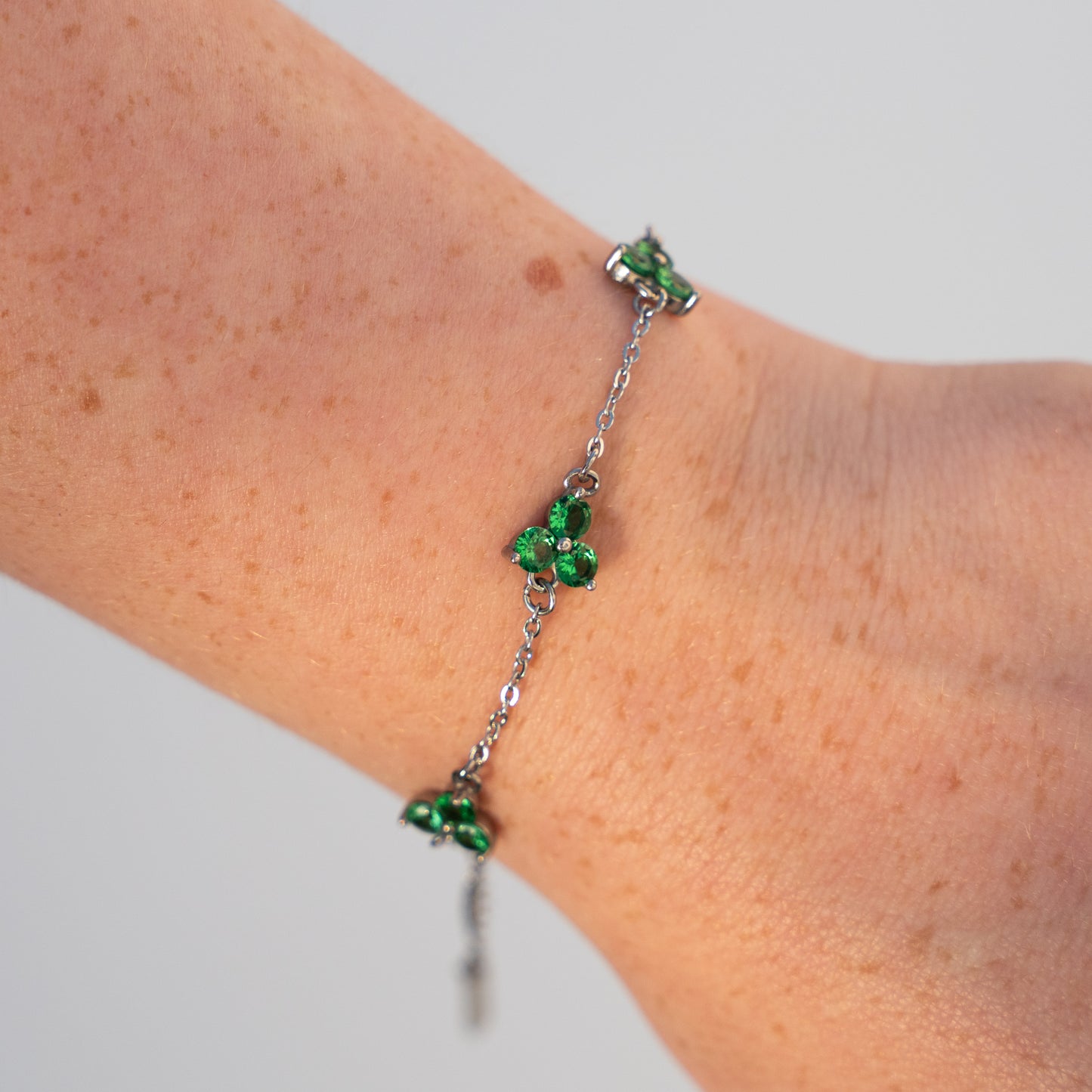 Silver bracelet with green gemstones on a wrist against a neutral background