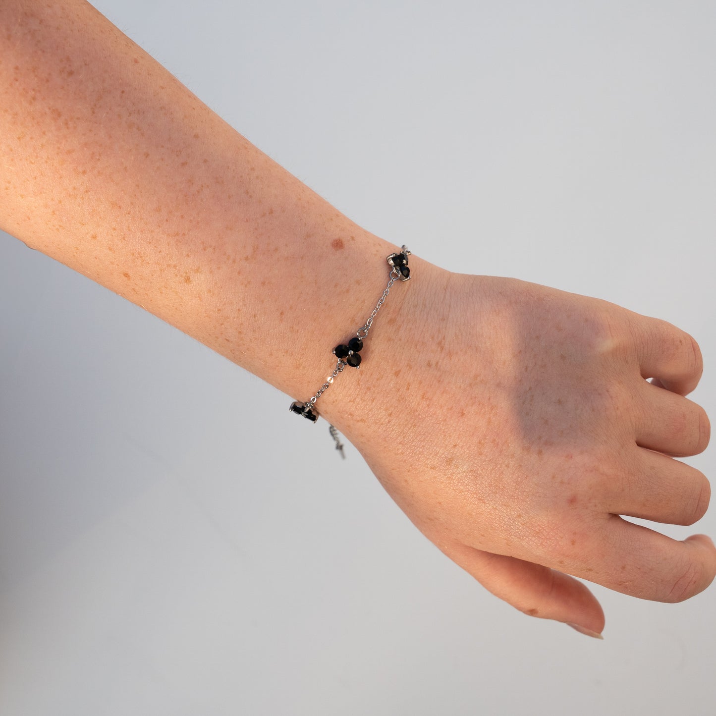 Hand wearing a silver bracelet with black gemstones on a plain background