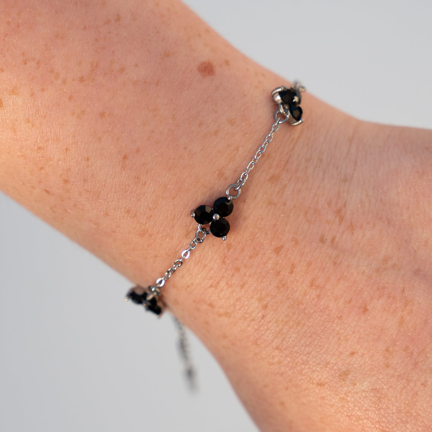 Silver bracelet with black gemstones on a wrist against a neutral background