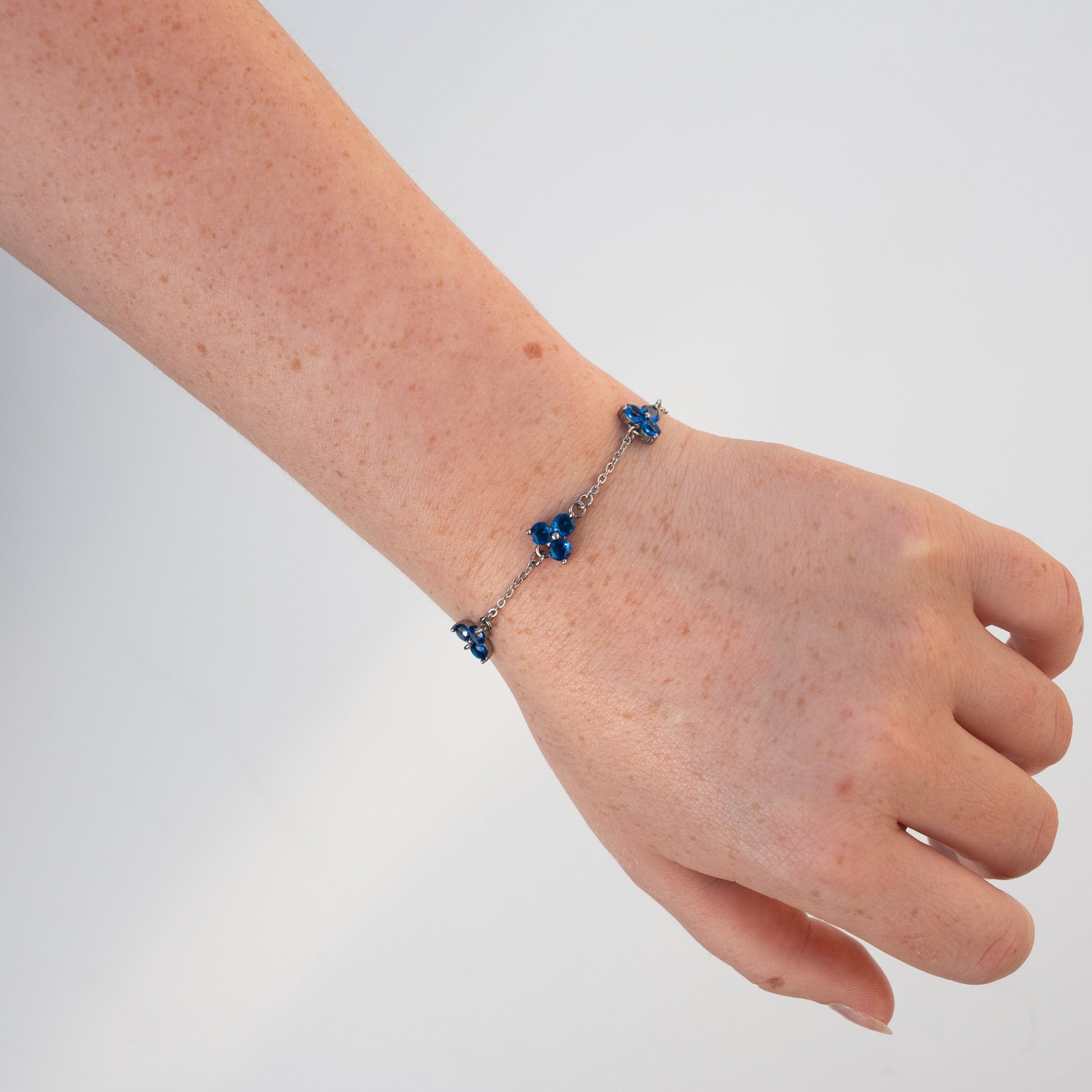 Hand wearing a silver bracelet with blue gemstones on a light background