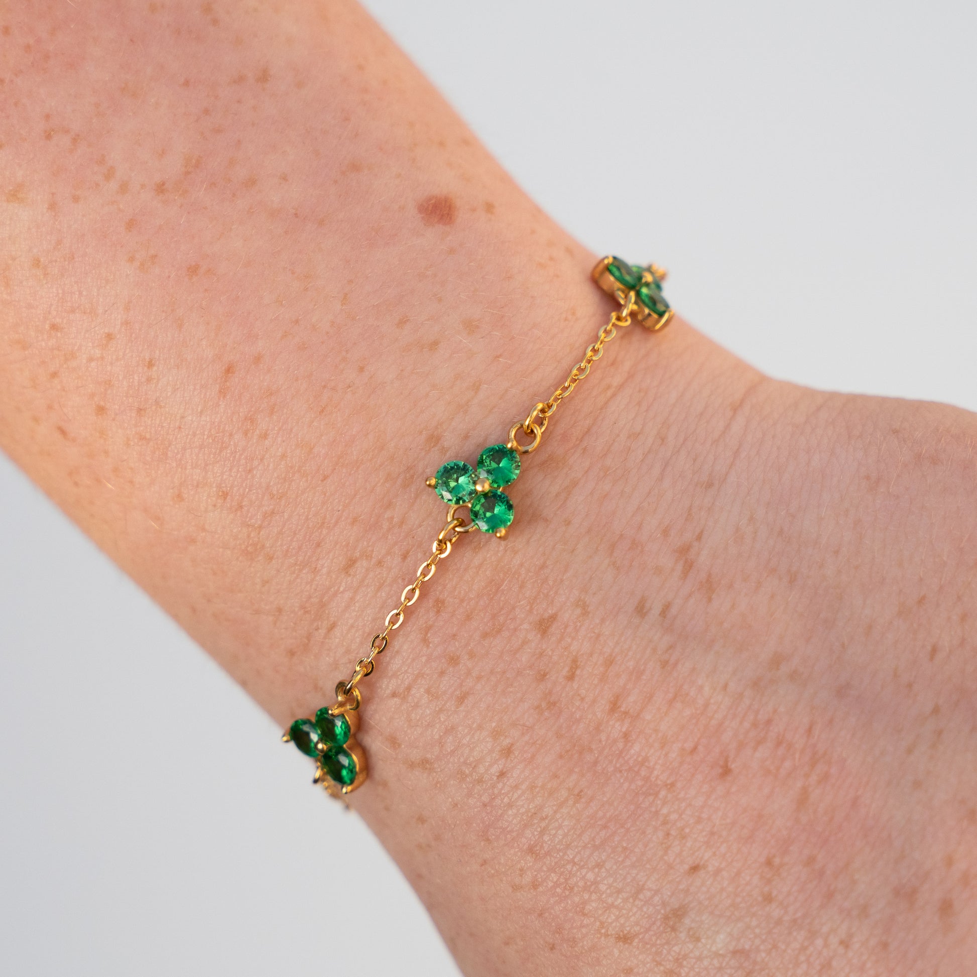 Gold bracelet with green gemstones on a wrist against a light background