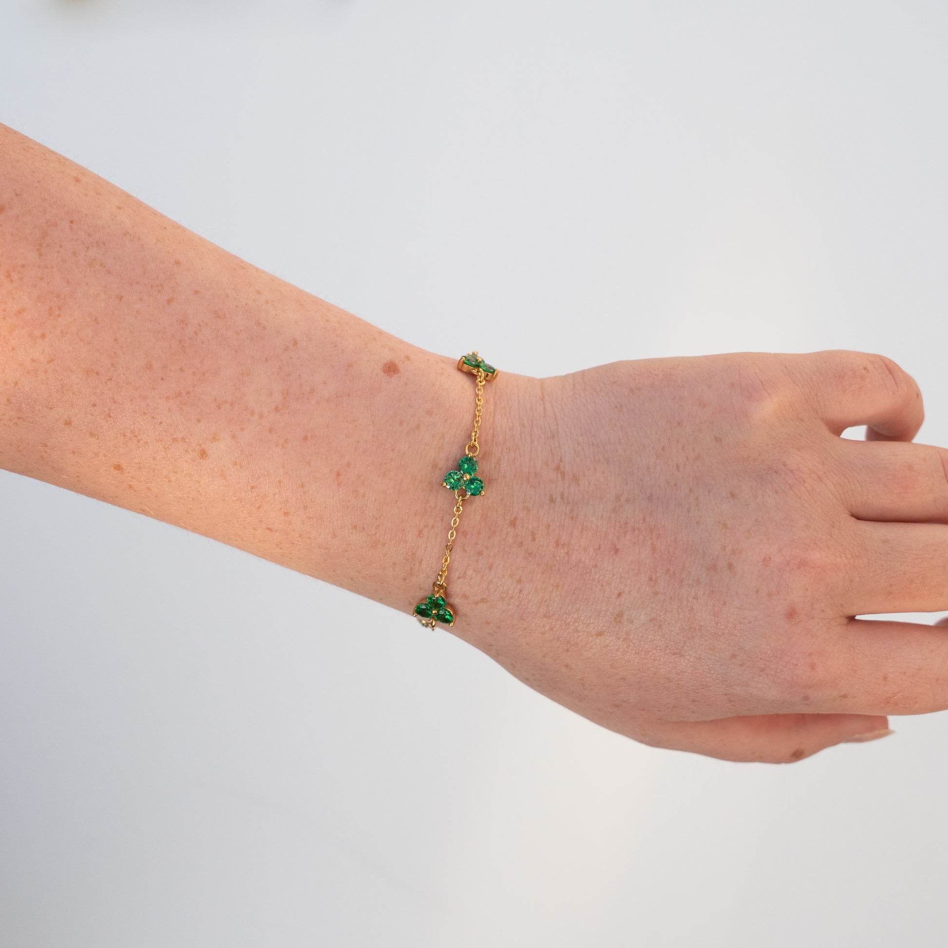 Gold bracelet with green clover charms on a wrist against a background