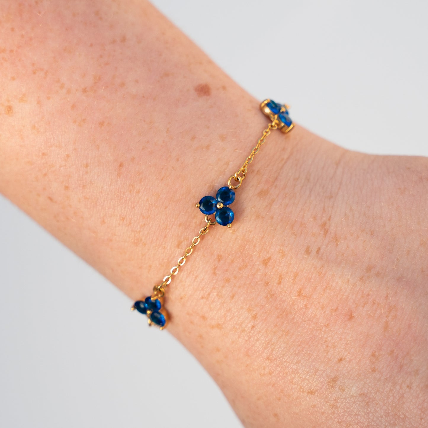 Gold bracelet with blue gemstones charms on a wrist against a light background
