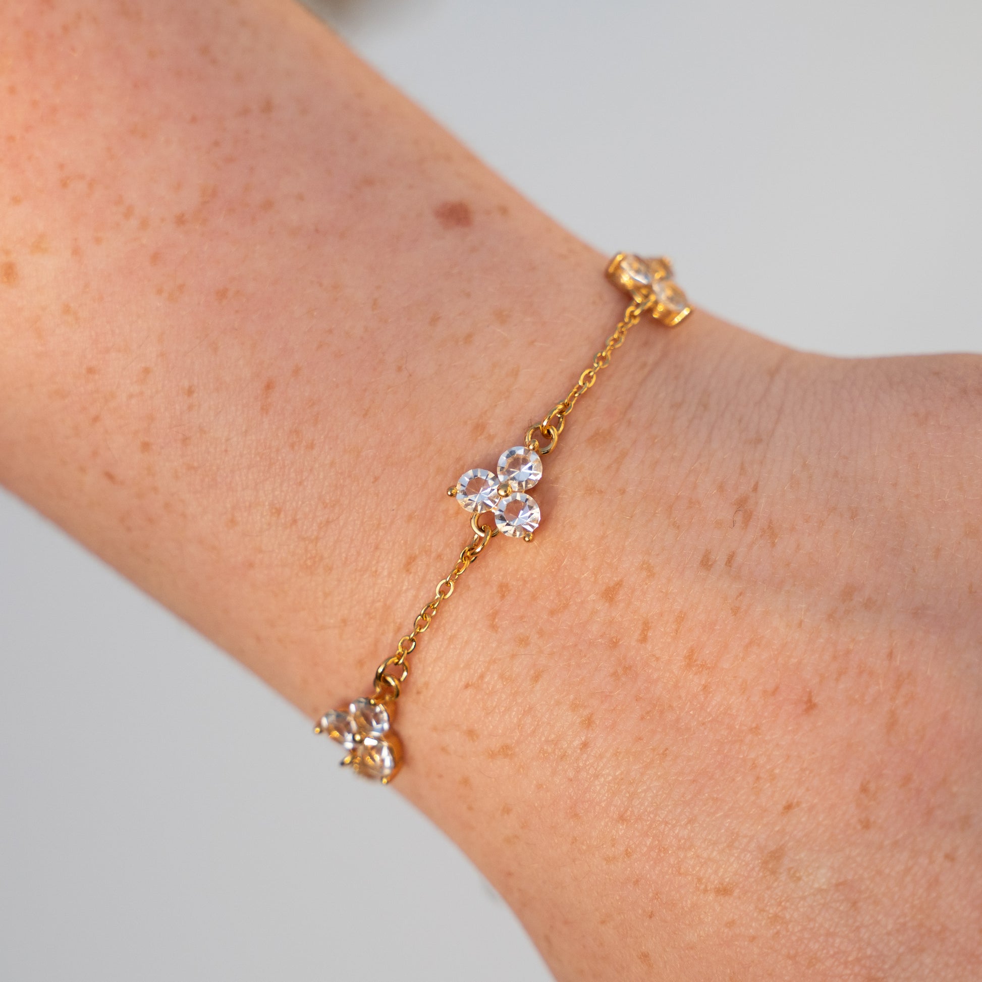 Gold bracelet with diamond-like white gemstones on a wrist against a neutral background