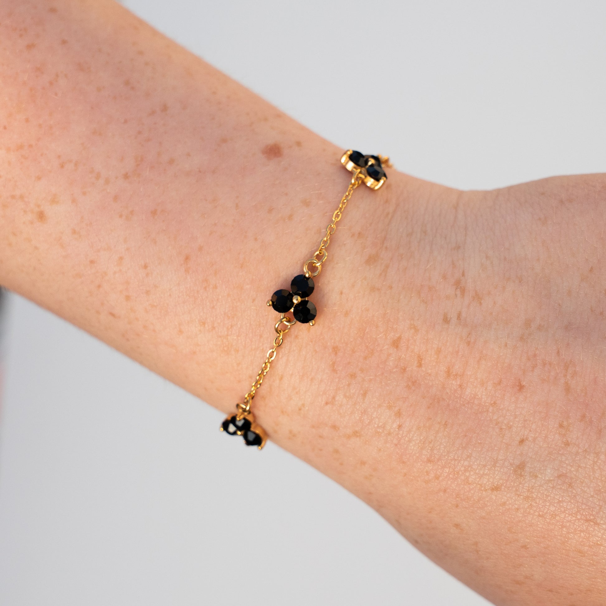 Gold bracelet with black gemstones on a wrist against a light background