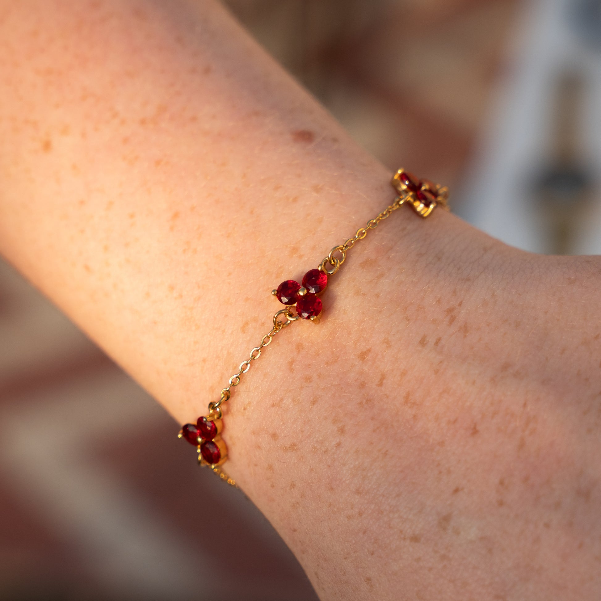Gold bracelet with red gemstones on a wrist against a blurred background